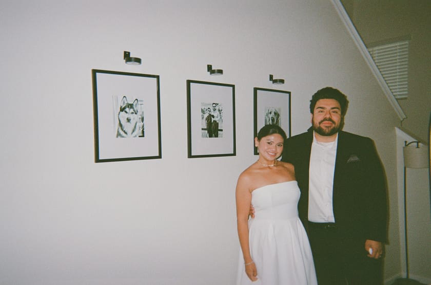 Film photo: the newlyweds beside their gallery wall of framed dog portraits