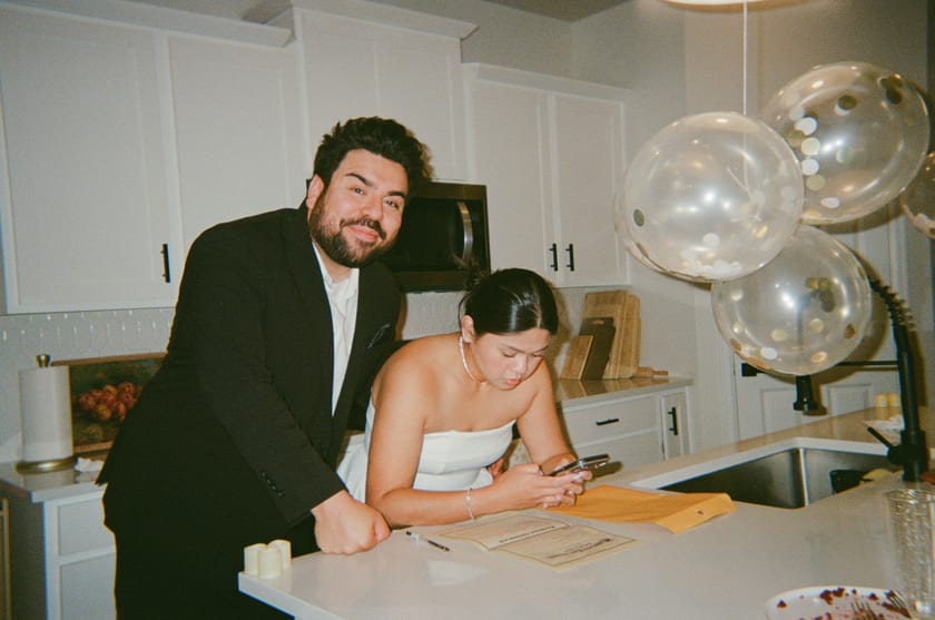 Film photo: signing the marriage license at the kitchen counter under gold balloons