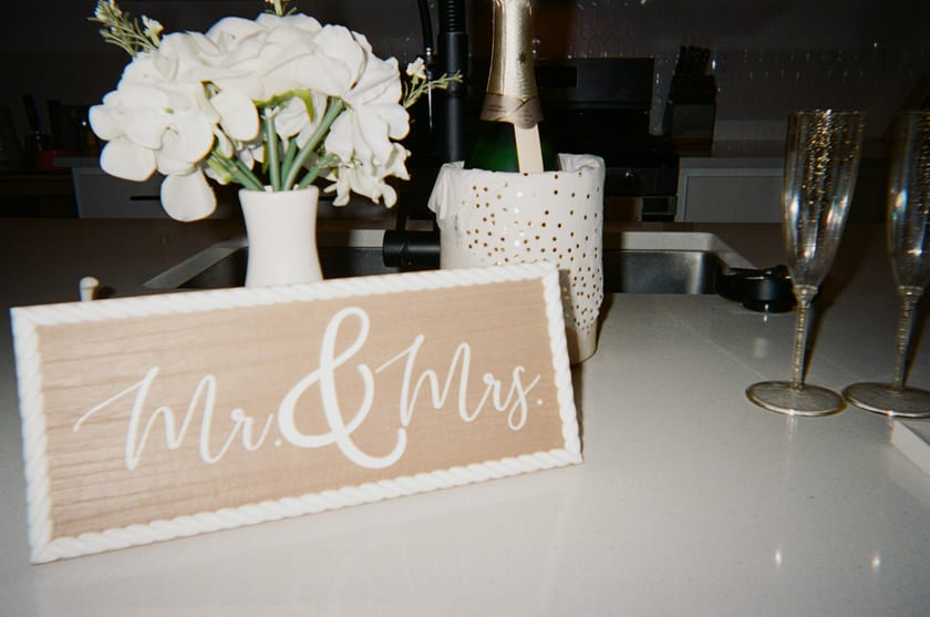 Film photo: white roses, champagne, and a wooden 'Mr & Mrs' sign