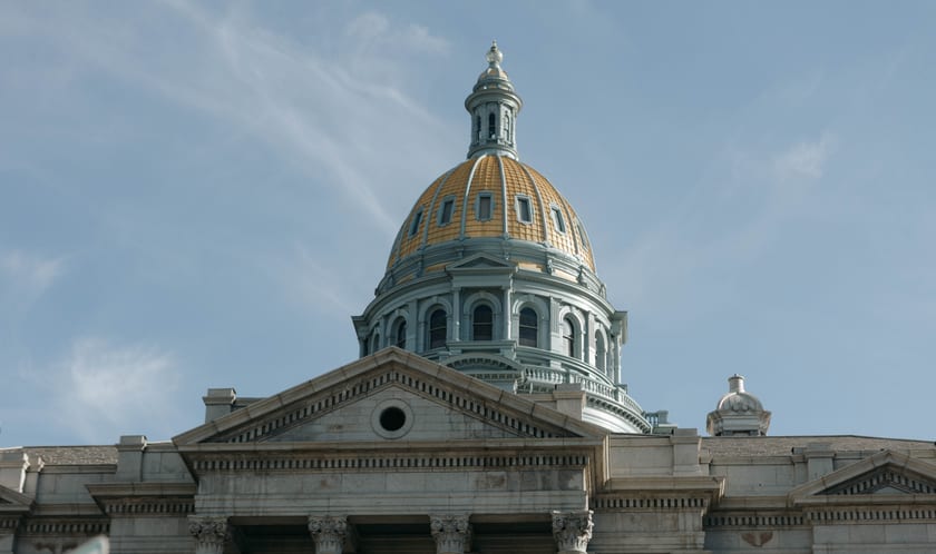 The gold-leafed dome of the Colorado State Capitol against a soft blue Denver sky