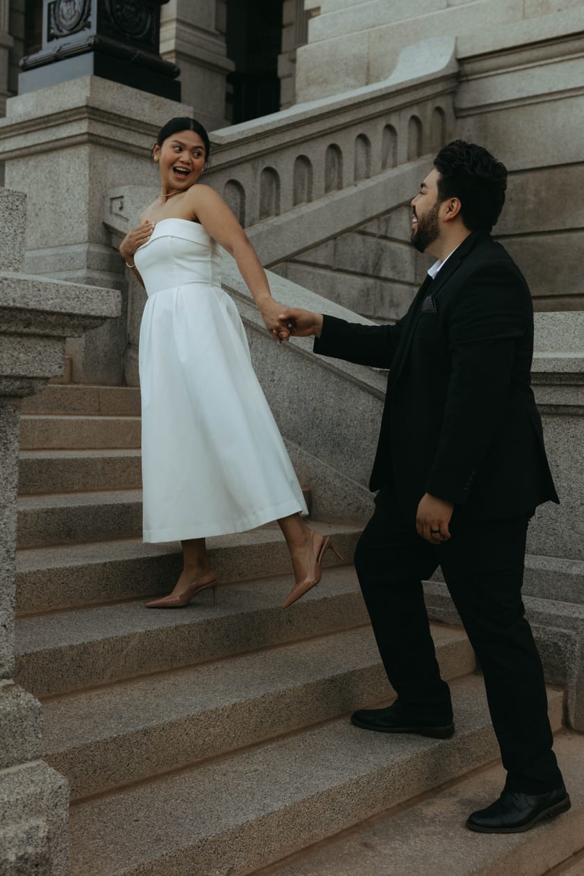 Ann glances back at Chris mid-laugh as they climb the Capitol steps hand in hand