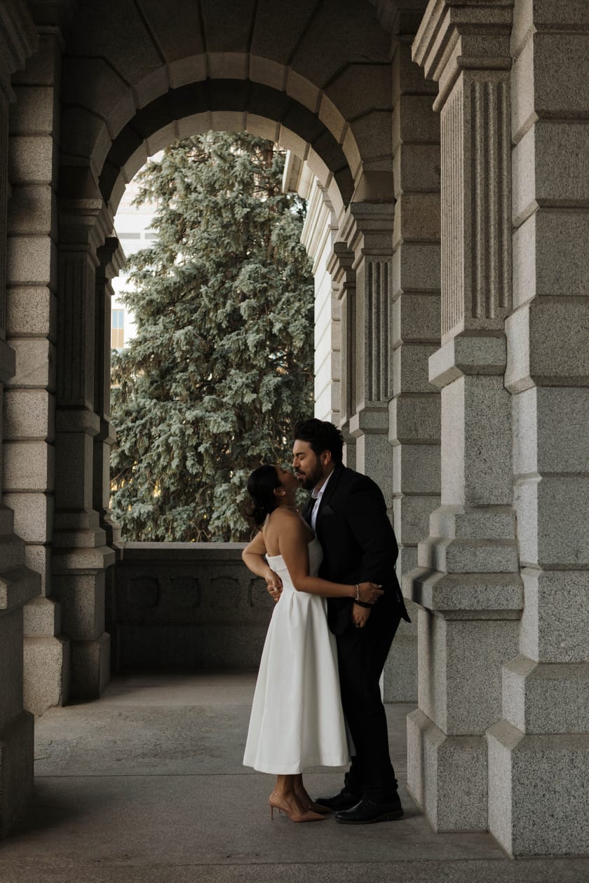 An embrace under the arch, evergreen boughs beyond