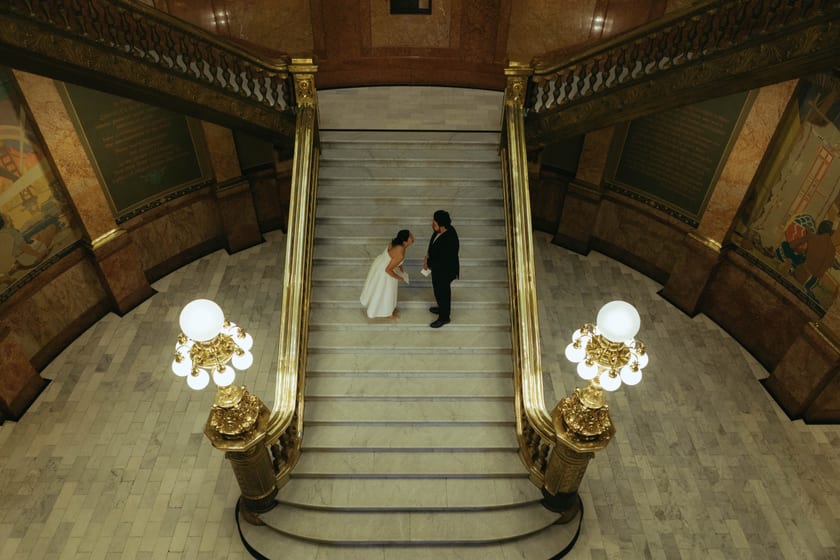 Reading vows at the base of the grand staircase, brass lamps glowing