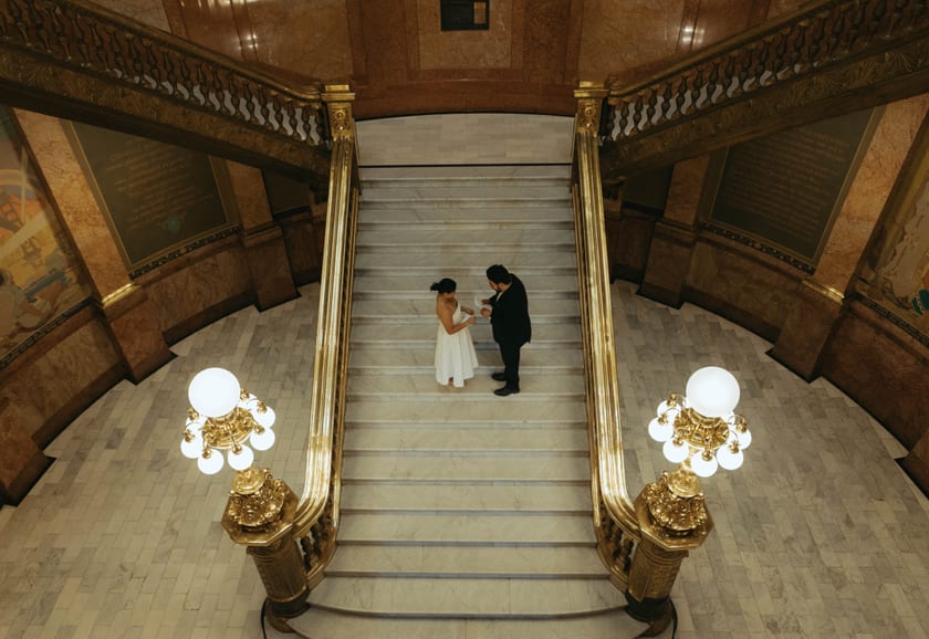 The stair hall in full: gilded railings, glowing globes, and a wedding of two