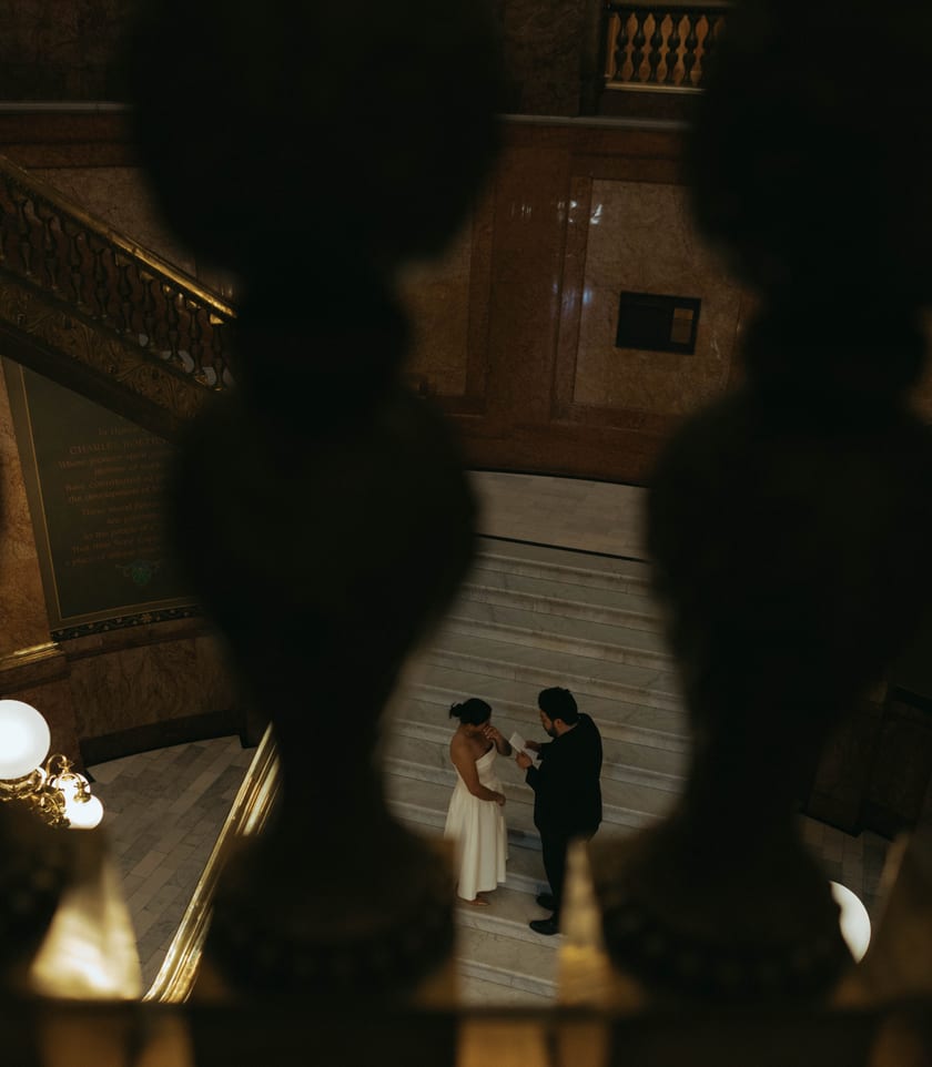 Glimpsed through the brass balustrade, reading vows by lamplight