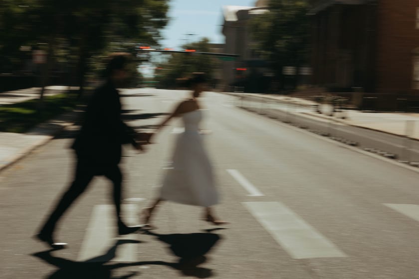 Crossing the street in motion blur, newly married and mid-laugh